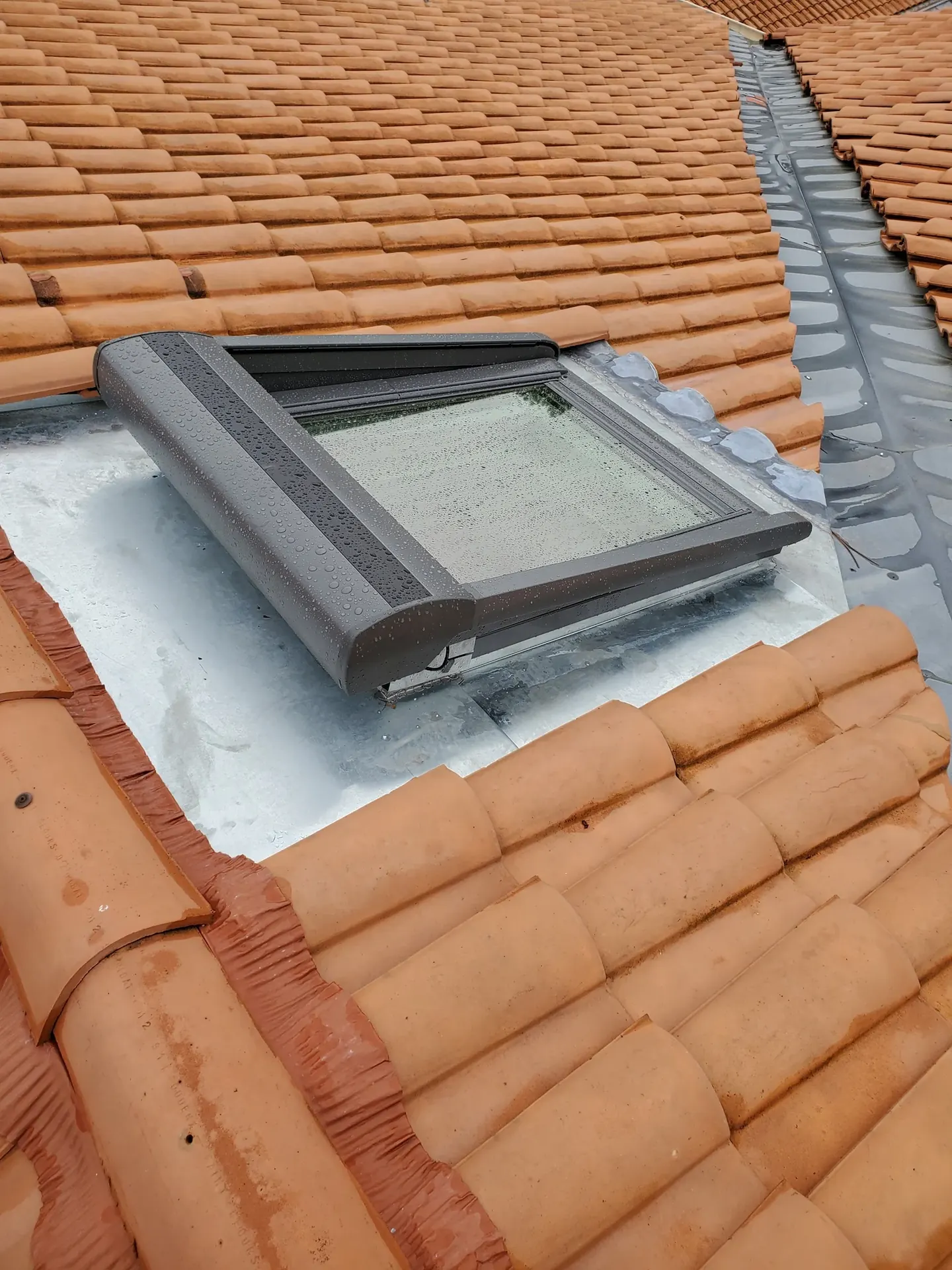 Fenêtre de toit posée avec son raccord en zinc sur une toiture en tuiles